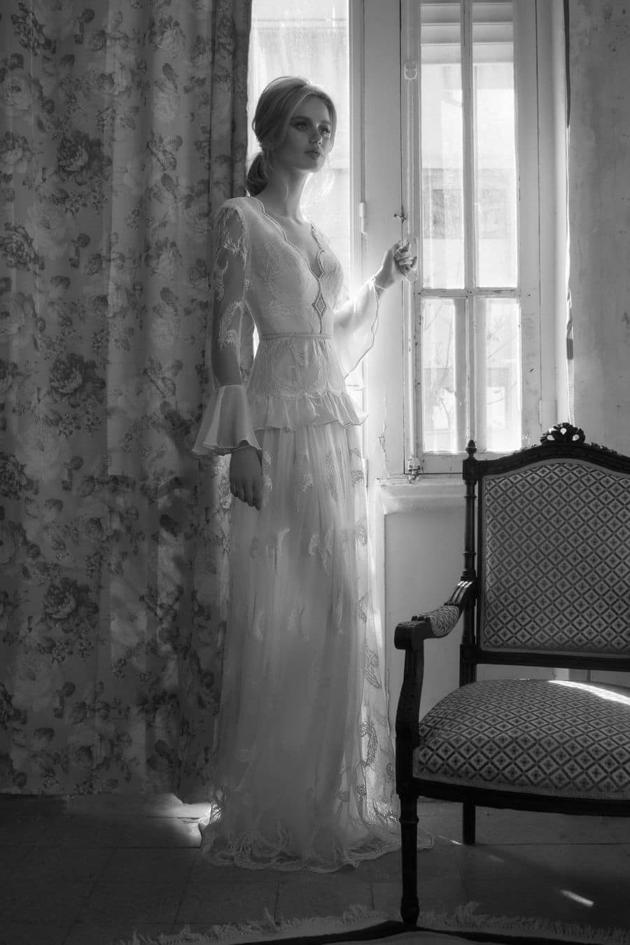 Bruid voor raam in bruidsjurk met parels en italiaans kant