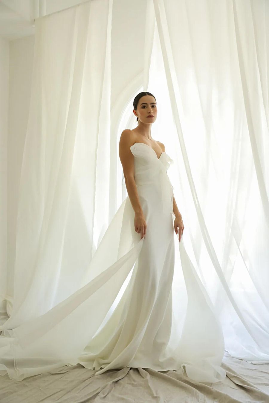 Bride standing in minimal fitted wedding dress with structured organza top and overskirt